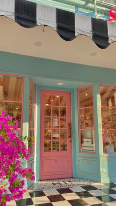 a pink and blue store front with flowers in the foreground on a checkered tile floor