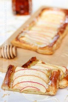 two slices of apple pie on a cutting board with honey and syrup in the background