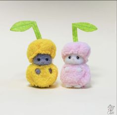 two small stuffed animals sitting next to each other on a white surface with one holding a green leaf