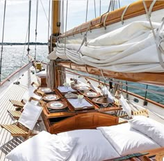 the deck of a sailboat with white linens and pillows on it, along with place settings