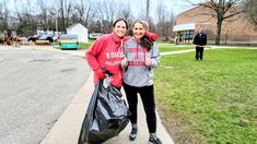 two people standing on the sidewalk with trash bags