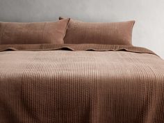 a bed with brown sheets and pillows on top of it, in front of a gray wall