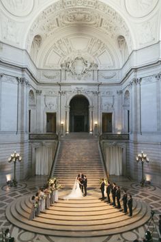 a bride and groom are standing on the stairs in front of an ornate building with chandeliers