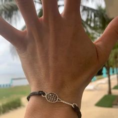 a person's hand with a bracelet on it and palm trees in the background