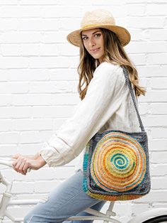 a woman riding a bike with a multicolored bag on it