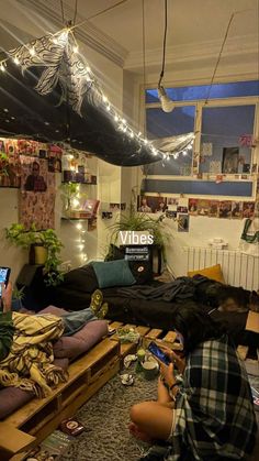 two people sitting on the floor in a room with lights strung from the ceiling above them