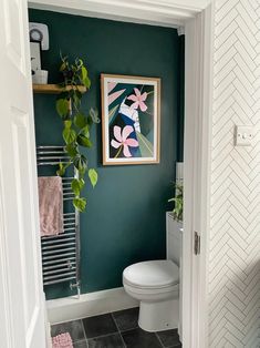 a white toilet sitting next to a green wall in a bathroom under a framed painting