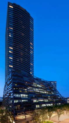 a very tall building sitting next to a park at night with people walking around it