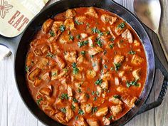 a pan filled with meat and sauce on top of a wooden table