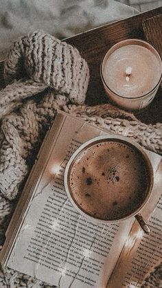 a cup of coffee on top of an open book with a lit candle next to it