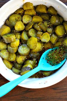 a white bowl filled with pickles and seasoning on top of a wooden table