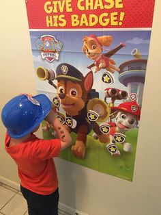 a young boy in red shirt and blue helmet playing with paw patrol poster on wall