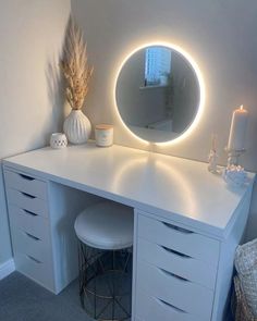 a white vanity with a round mirror and lights on it's sides, next to a stool