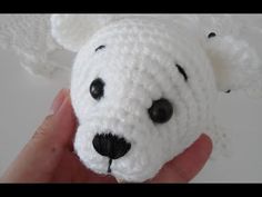 a crocheted white teddy bear is held in someone's hand with black eyes