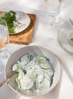 a bowl full of cucumbers sitting on top of a table next to glasses