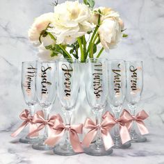 four champagne flutes with pink bows and white flowers in the vase on a marble surface