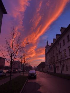 a car is parked on the street in front of some buildings and trees at sunset