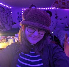 a woman wearing glasses and a knitted hat smiles at the camera in her bedroom