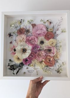 a person holding up a white frame with flowers in it