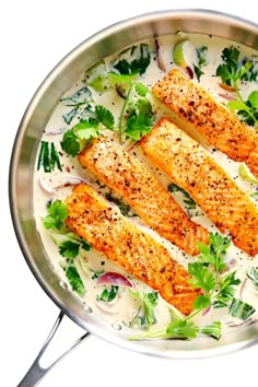 three salmon fillets in a pan with white sauce and garnishes on top