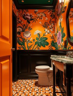 an orange and black bathroom with flowers on the wall, toilet and sink area in front of mirror