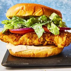 a chicken sandwich with lettuce and tomato slices on a black plate next to a blue background