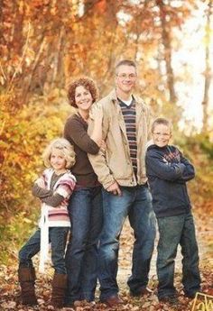 a family posing for a photo in the woods with autumn leaves on the ground and trees behind them