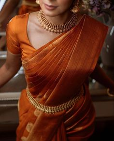 a woman in an orange sari with gold jewelry on her neck and hands behind her back