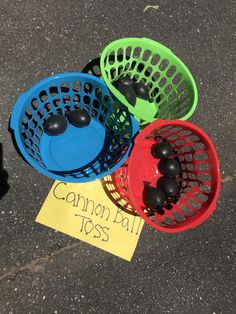 four different colored plastic baskets sitting on the ground next to a sign that says cannon ball toss