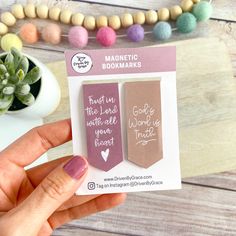 a hand holding up a magnet with some writing on it next to a potted plant