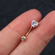 a person's hand holding a gold nose ring with a heart shaped diamond on it