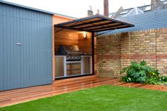 an outdoor kitchen is built into the side of a brick wall and has grass in front of it