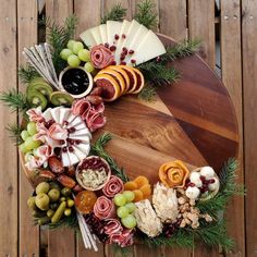 a platter with cheeses, meats and grapes on it is displayed in front of a wooden fence