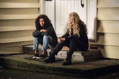 two young women sitting on steps in front of a house, one is looking at the camera