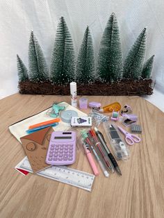 a wooden table topped with lots of office supplies next to a pine tree filled with pencils and markers