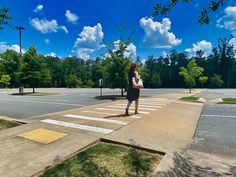 a woman standing on the side of a road next to a cross walk and trees