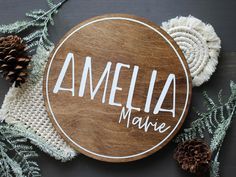 a wooden sign with the word amelie marie written on it next to pine cones and yarn