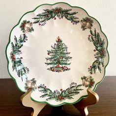 a white plate with green trimmings and christmas decorations on it sitting on a wooden table