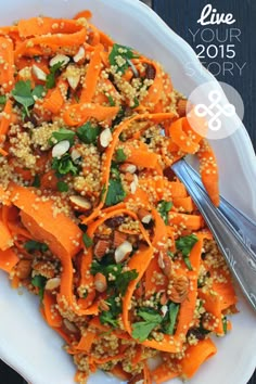 a white plate topped with carrots and nuts next to a silver fork on top of a wooden table