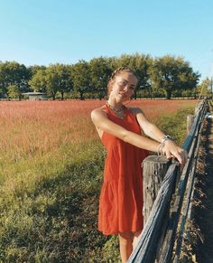 a woman in an orange dress leaning on a fence