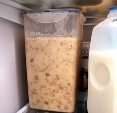 a plastic container filled with liquid next to a bottle of milk on top of an open refrigerator door