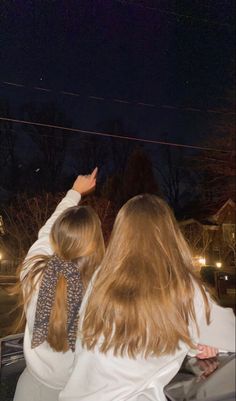 two girls are flying a kite in the night sky with one girl pointing at something