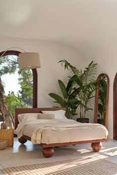 a bed sitting in the middle of a bedroom next to two large arched windows and a potted plant