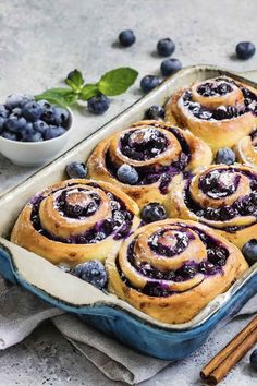 blueberry cinnamon rolls in a baking dish with fresh blueberries and cinnamon sticks on the side