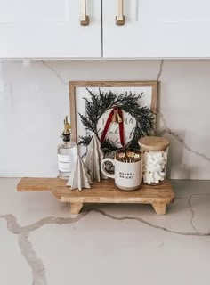 an assortment of christmas items on a wooden shelf in a kitchen with white cabinets and marble countertops