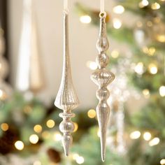 two silver ornaments hanging from strings in front of a christmas tree