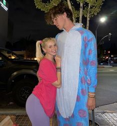 a man and woman dressed in costumes standing next to each other on the sidewalk at night