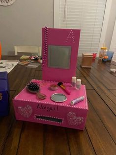 a pink vanity with mirror and other items on top of it sitting on a wooden table