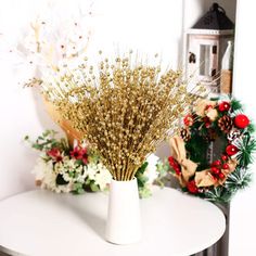 a white vase filled with lots of flowers on top of a table next to a wreath