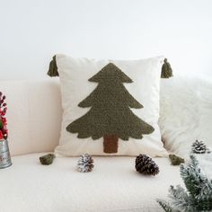 a christmas tree pillow sitting on top of a white couch next to evergreen cones and pine cones